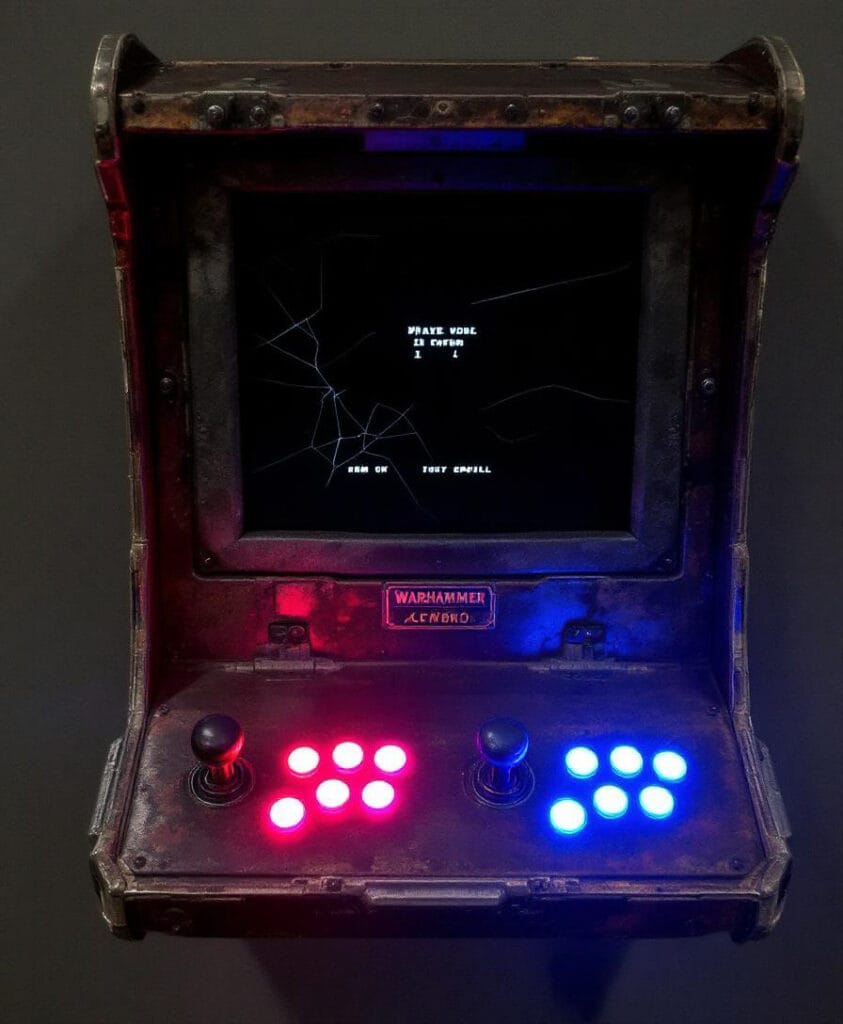 Wandmontierter Arcade-Spielautomat mit einem Bildschirm und mehreren Steuerknöpfen in rot und blau.