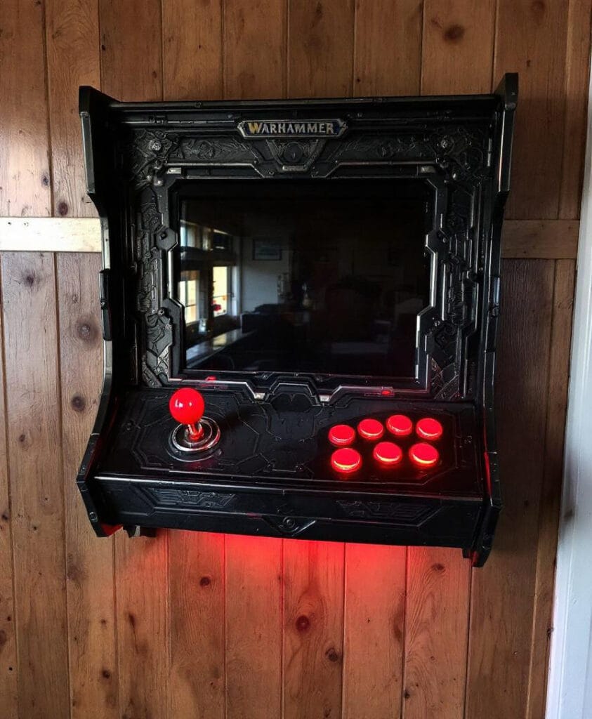 Wandmontierter Arcade-Spielautomat mit Warhammer-Logo und roten Tasten.