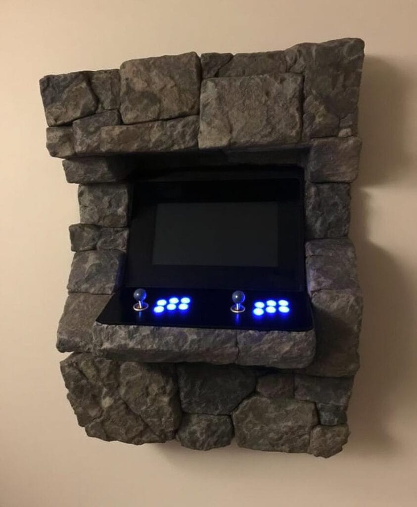 Wandmontierter Arcade-Spielautomat mit einem Rahmen aus Stein und einem schwarzen Bildschirm.